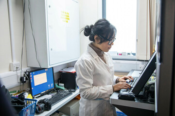 Scientist working at computer in lab of a medical practice, UK