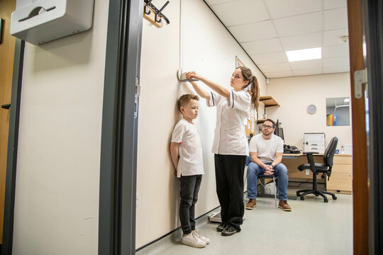 Child being measured during a medical check-up as father observes.