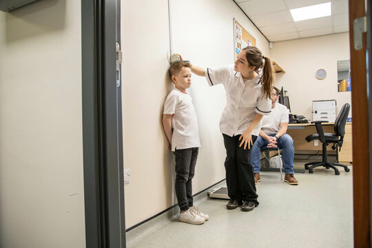 Child being measured during a medical check-up as father observes.