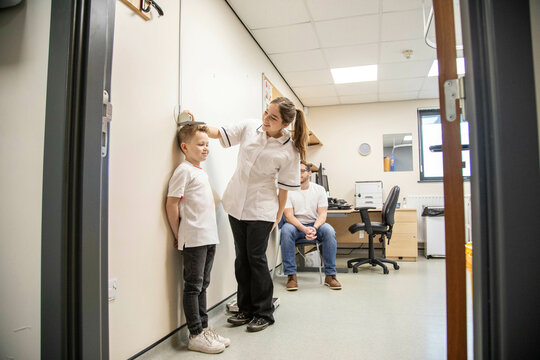 Child being measured during a medical check-up as father observes.