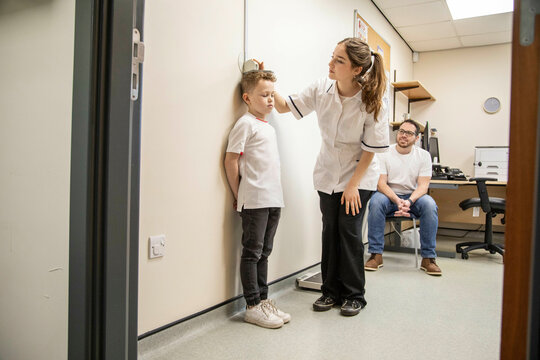 Child being measured during a medical check-up as father observes.