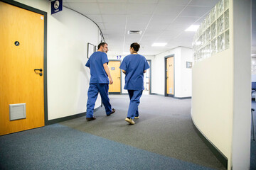 Two healthcare workers walking in a hospital corridor, medical practice UK