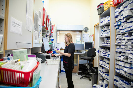 Pharmacist working at a computer in a pharmacy surrounded by medication shelves.