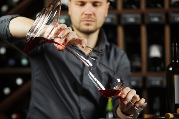 Sommelier pouring wine into glass from mixing bowl. Male waiter