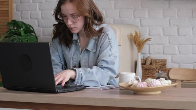 Engrossed in her work, a woman uses her laptop in a bright, minimalist kitchen, highlighting the adaptability required in today's hybrid work models.