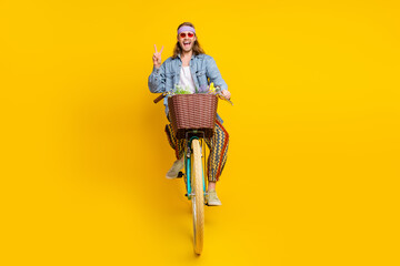 Full body portrait of cool young guy ride bike show v-sign wear denim shirt isolated on yellow...