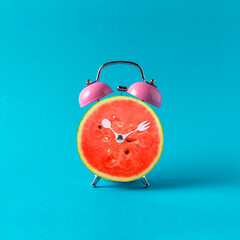 Pink alarm clock watermelon on blue background. Minimal concept.