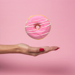 Female hand with flying delicious donut on pink background. Mini