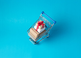 Gift boxes in shopping cart on blue background. Minimal sale con