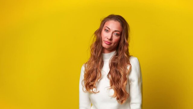 Bored woman take off Santa hat and throwing it over yellow background. Disheartened young female model is standing in studio.