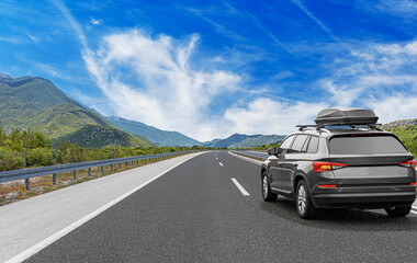 Travel car drives along the highway against the backdrop of rocky mountains on a sunny day.