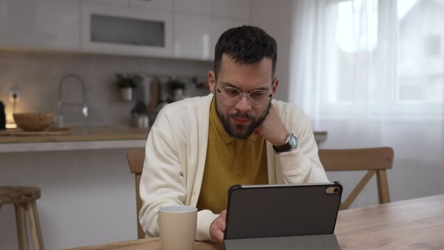 Adult caucasian man sit at kitchen look at tablet and have headache