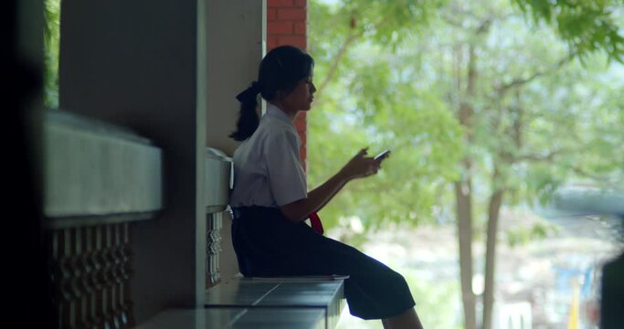 A silhouette scene of a young Asian high school girl with a highly private world or introvert, casually scrolling through social media on her smartphone in the evening after school.