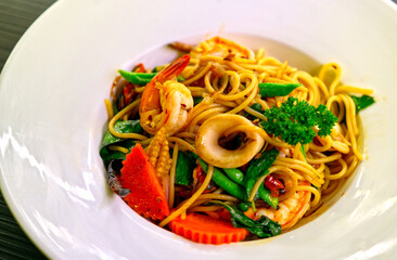 Close up the fusion food of Thai and Italian style, Spaghetti Pad Kee Mao Ta Lay or Stir Fried spaghetti with spicy Thai herbs with seafood. Close up food image in beautiful white serving dish.