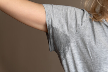 Close-up of a young woman shows a wet armpit on a gray T-shirt. Concept of health, sports