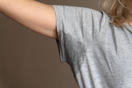 Close-up of a young woman shows a wet armpit on a gray T-shirt. Concept of health, sports