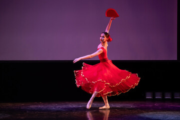ballerina in a red dress performs a variation from the ballet Don Quixote on the theater stage.