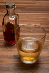 木目テーブルの上の丸氷のウィスキーオンザロックとミニボトル