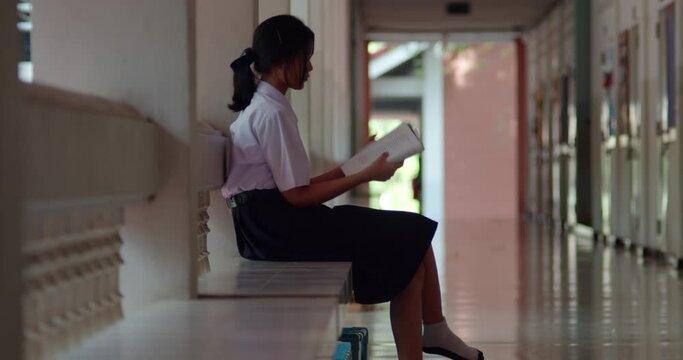 An Asian high school student girl in white uniform sits and read a book anxiously to prepare for exams in the evening after school while waiting for her parent to take her home.