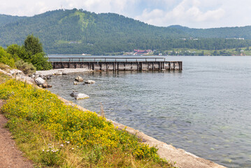 Coast of Baikal Lake on a sunny summer day. View of a wooden pier in the village of Port Baikal on the shore of the lake. Summer travel and outdoor recreation. Beautiful landscape. Nature background