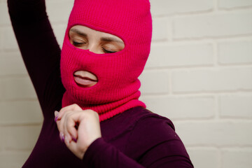 A woman wearing a bright pink balaclava dances energetically, striking unique poses with her hands...