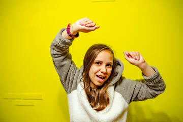 Woman in Cozy Sweater Dancing Against Bright Yellow Wall During Daytime