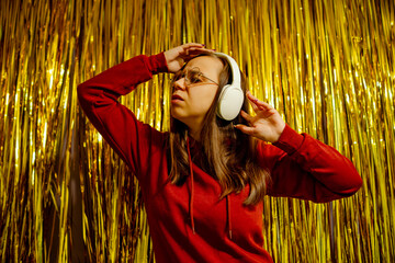 A woman wearing glasses and headphones energetically dances in front of a shimmering gold backdrop.
