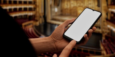 Hand holding a phone with a blank screen against a theater backdrop