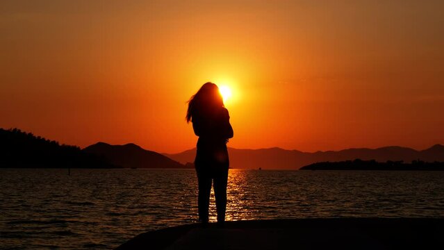 Girl alone at sunset. Silhouette of a lonely girl on the sea promenade at sunset.