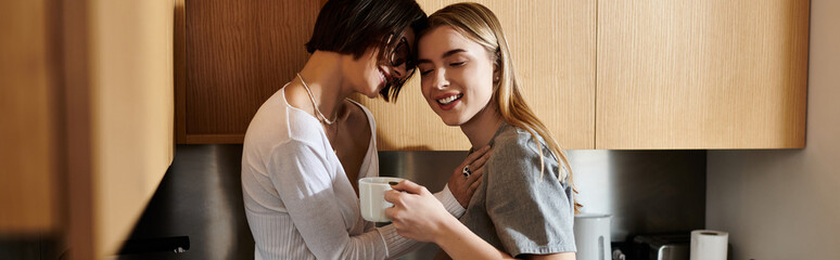A young lesbian couple standing together in a hotel kitchen, holding coffee and engaging in conversation. - Powered by Adobe