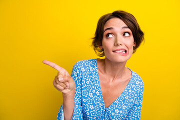 Photo of confused woman with bob hairstyle dressed print blouse indicating look empty space biting lip isolated on yellow color background