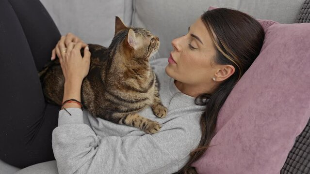 Young woman relaxing at home with her pet cat on a couch, enjoying a quiet moment together in a cozy living room.