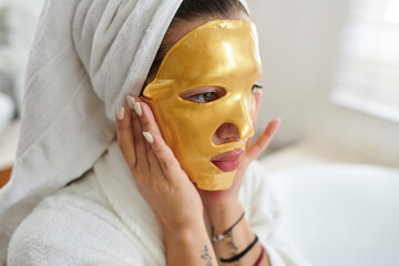 Woman applying revitalizing face mask after shower