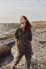 Woman in olive green jumpsuit standing on cliff in desert landscape during adventure travel trip