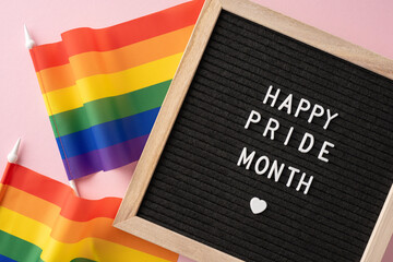 Happy Pride Month message displayed on a letter board with two rainbow flags on a pink background...