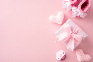 Pastel pink baby shower concept with gift box, knitted hearts, baby booties, and pacifier on pink background