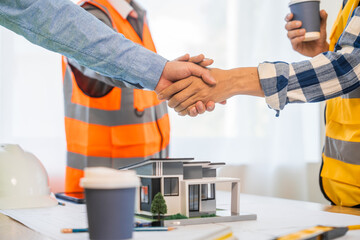 An architect engineer meeting is taking place at a desk covered with blueprints. They are...