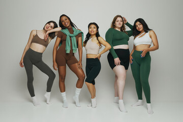 Diverse group of five women standing together in athleisure wear, showcasing different body types...