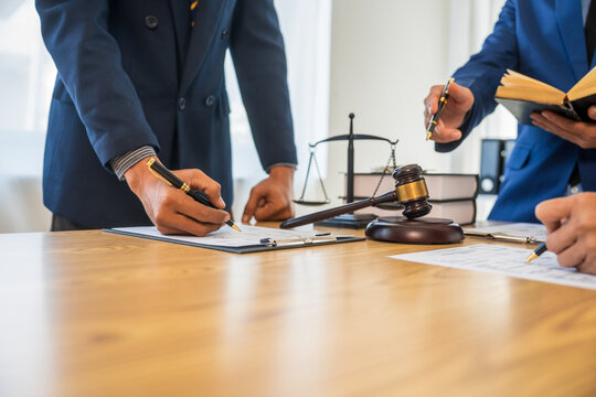 A team meeting of business people and a lawyer in formal suits is taking place at a desk, discussing a contract and various aspects of the law and litigation.