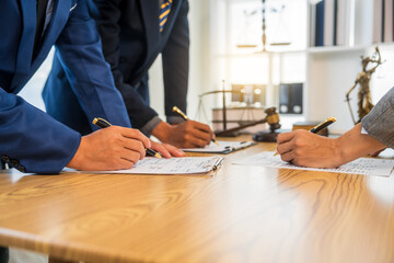 A team meeting of business people and a lawyer in formal suits is taking place at a desk,...