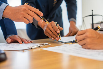A team meeting of business people and a lawyer in formal suits is taking place at a desk,...