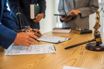 A team meeting of business people and a lawyer in formal suits is taking place at a desk, discussing a contract and various aspects of the law and litigation.