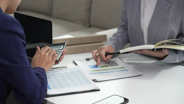 Two Asian businesswomen collaborate on stock market strategies and financial services, exchanging comments and suggestions on loan applications and investment opportunities.
