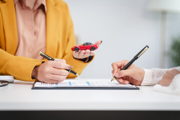 Asian businesswoman and a salesman discuss car sales, insurance, and financing with a customer at a desk, covering used car loans, premiums, deductibles, and various insurance coverage options.