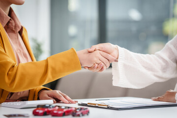 Asian businesswoman shakes hands with a salesman and customer at a desk, discussing car sales,...