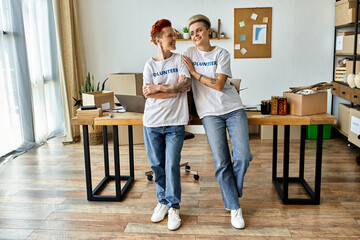 Two women in volunteer t-shirts standing in a room, working together for a charity cause with a...