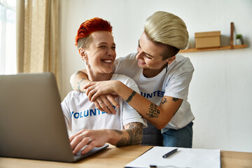 A man and a woman embrace while looking at a laptop, engaging in volunteer work with empathy and...