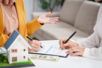 Asian businesswoman discusses home purchase contracts with clients at her desk, focusing on loans, mortgages, and other financial aspects of real estate transactions.