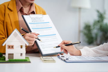 Asian businesswoman discusses home purchase contracts with clients at her desk, focusing on loans,...