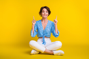 Full length photo of impressed girl dressed print blouse sit indicating at promotion empty space...